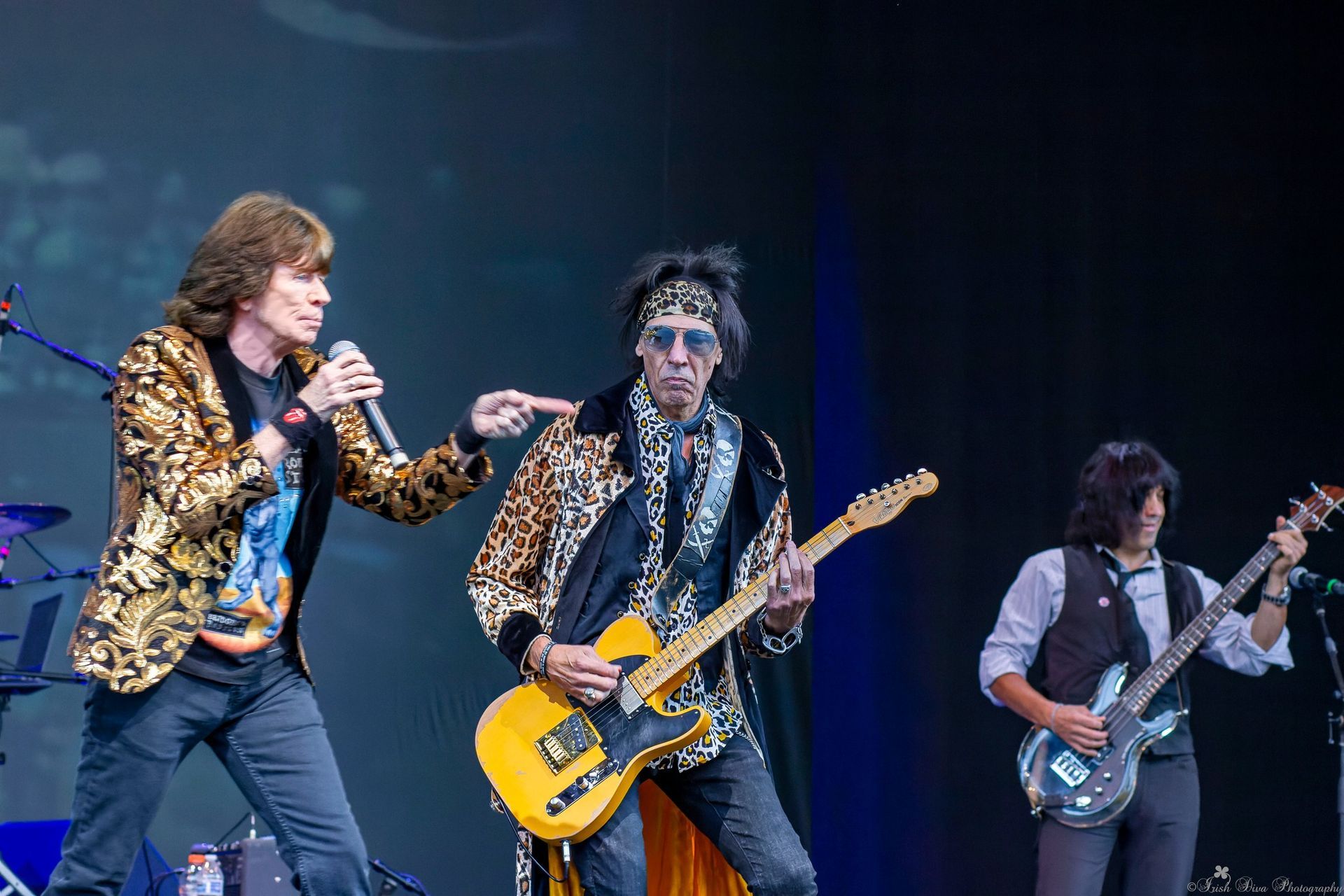 Three musicians perform onstage with guitars and microphones under blue lights