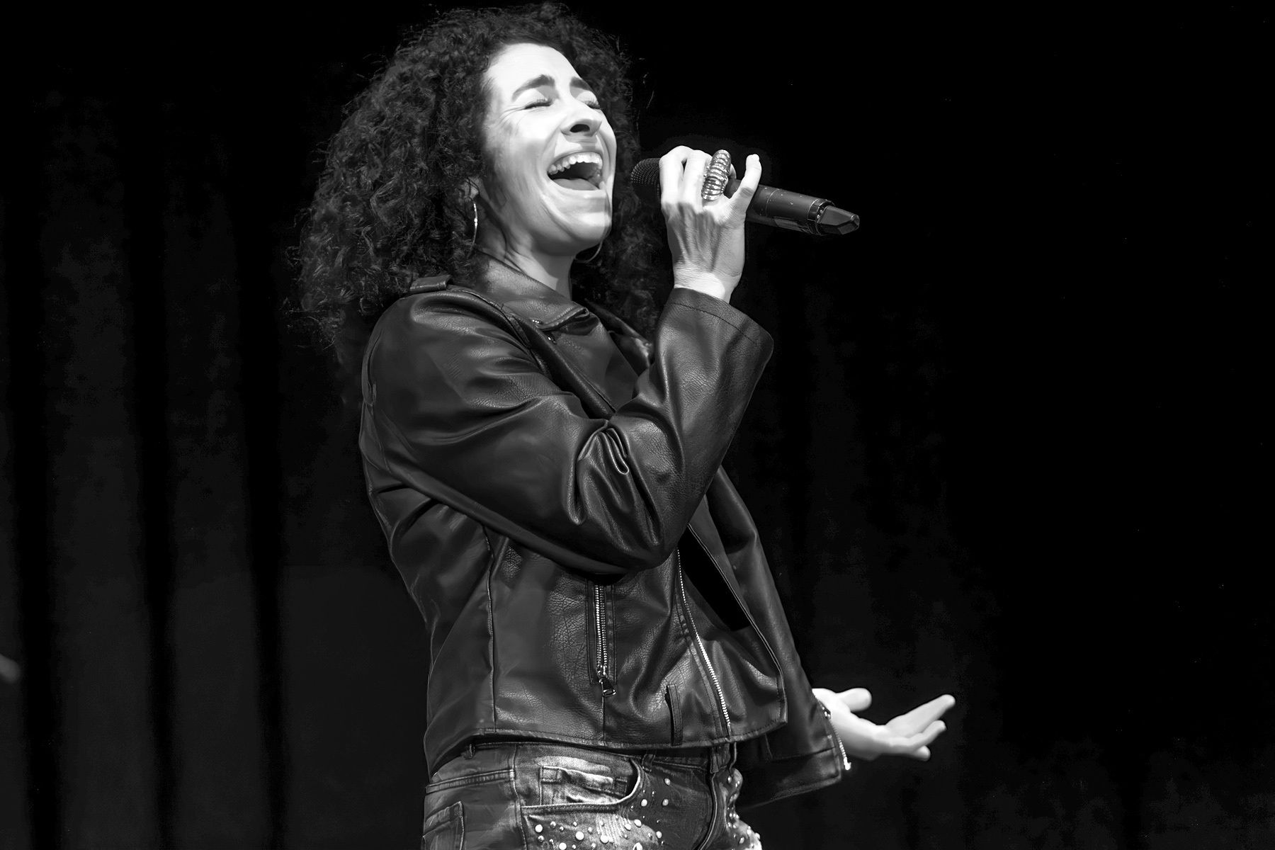 Singer performing onstage, holding a microphone and singing in a leather jacket.