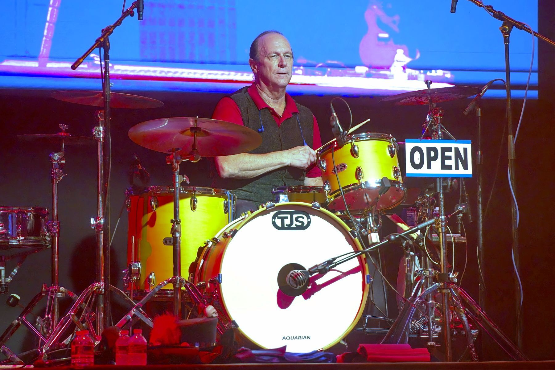 Drummer on stage playing a yellow drum kit with an OPEN sign beside him
