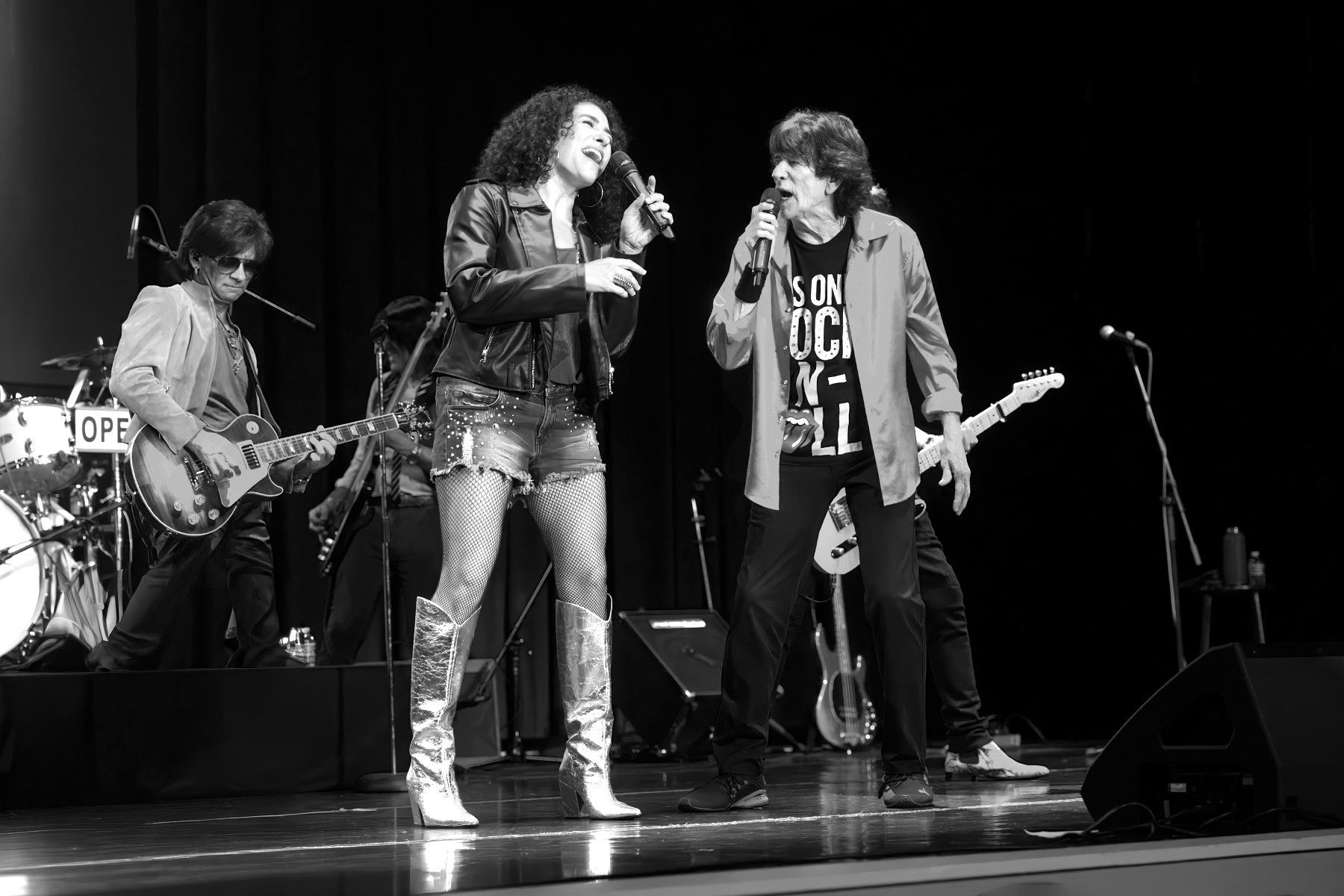 Black-and-white photo of three musicians performing on stage with guitars and microphones