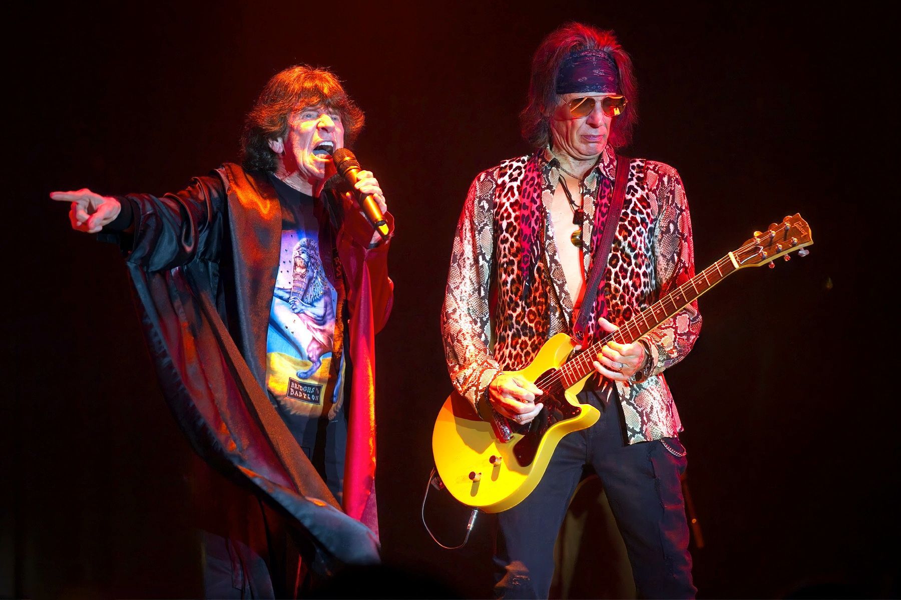 Two musicians performing on stage, one singing into a microphone and one playing a yellow guitar.