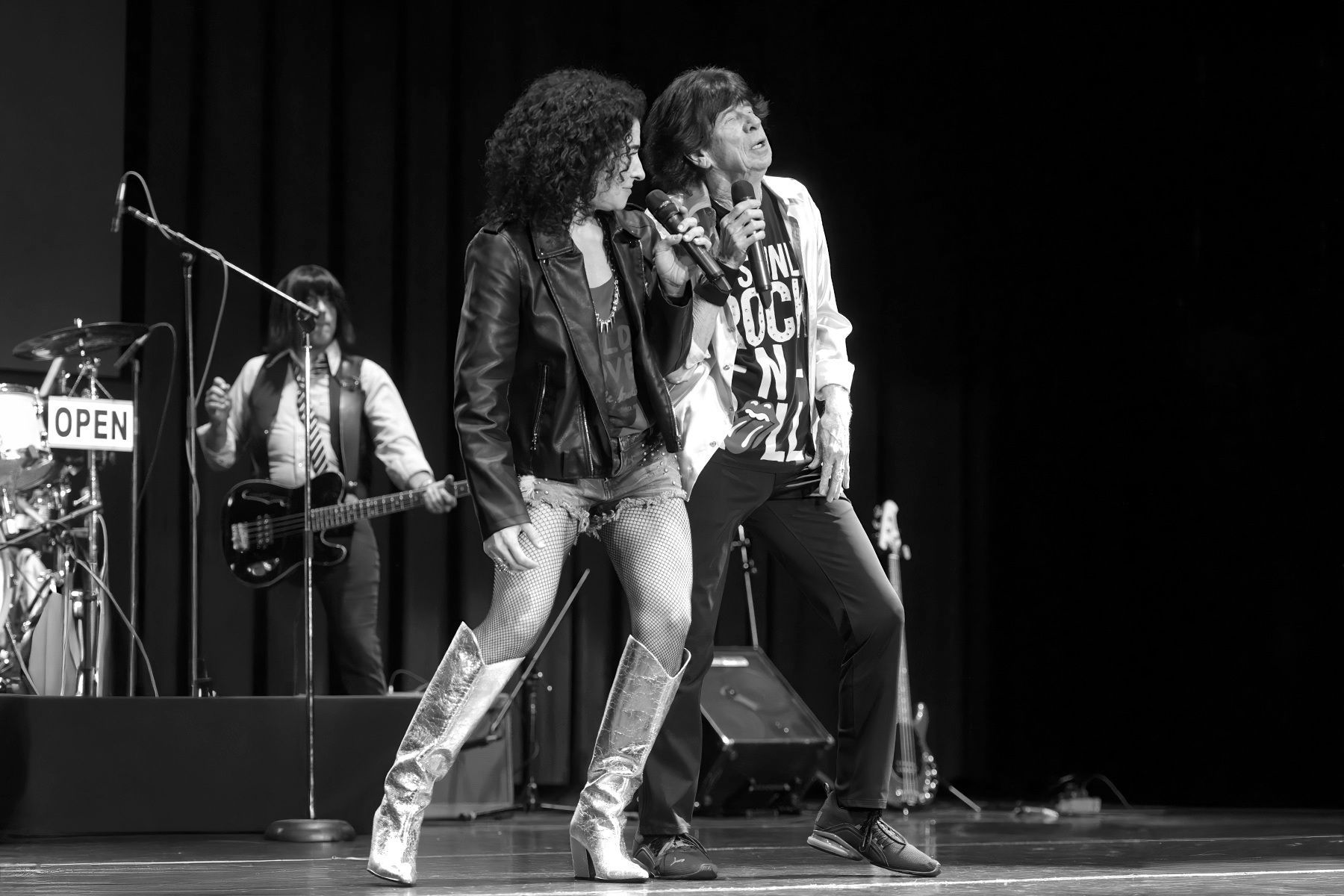 Three musicians perform on stage, with a vocalist and guitarist in the foreground and a keyboardist behind.