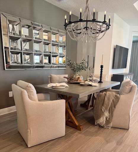 Dining room with square mirror, chandelier, table, and chairs. Table set with centerpiece and blanket.