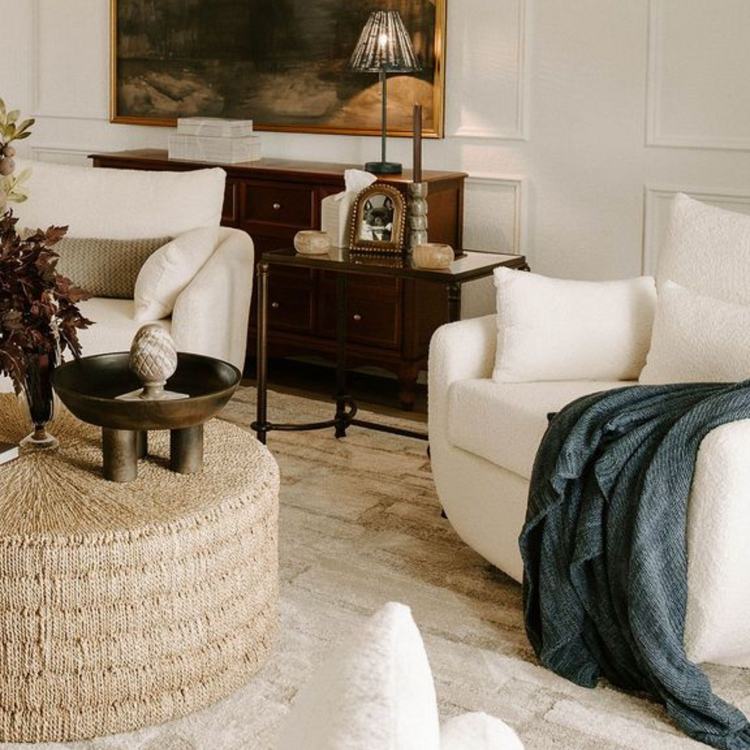 Cozy living room with cream-colored seating, wooden furniture, patterned rug, and a dark blue throw blanket.