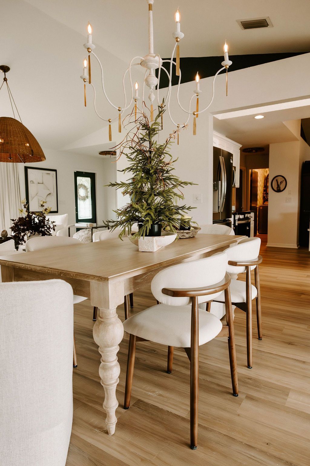 Dining room with a white chandelier, table, chairs, and small Christmas tree centerpiece.