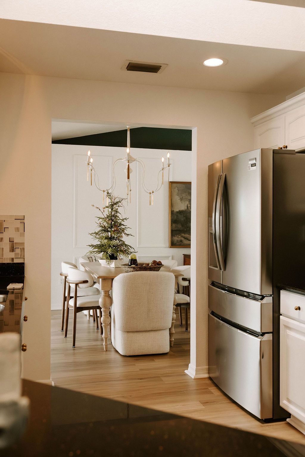 Dining room through doorway, Christmas tree, white walls, and stainless steel refrigerator.