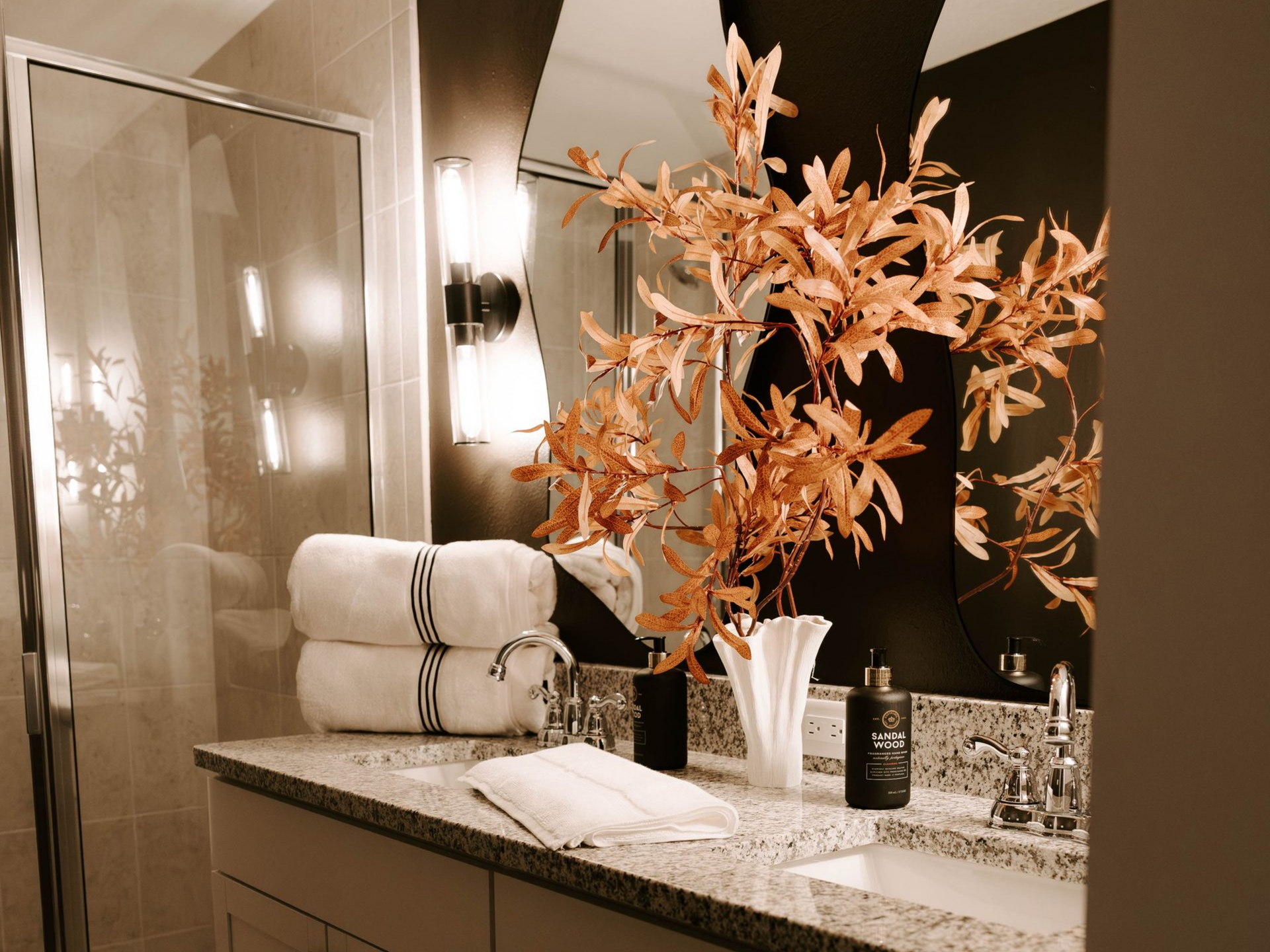 Bathroom with granite countertop, large mirror, and decorative orange branches in a vase.