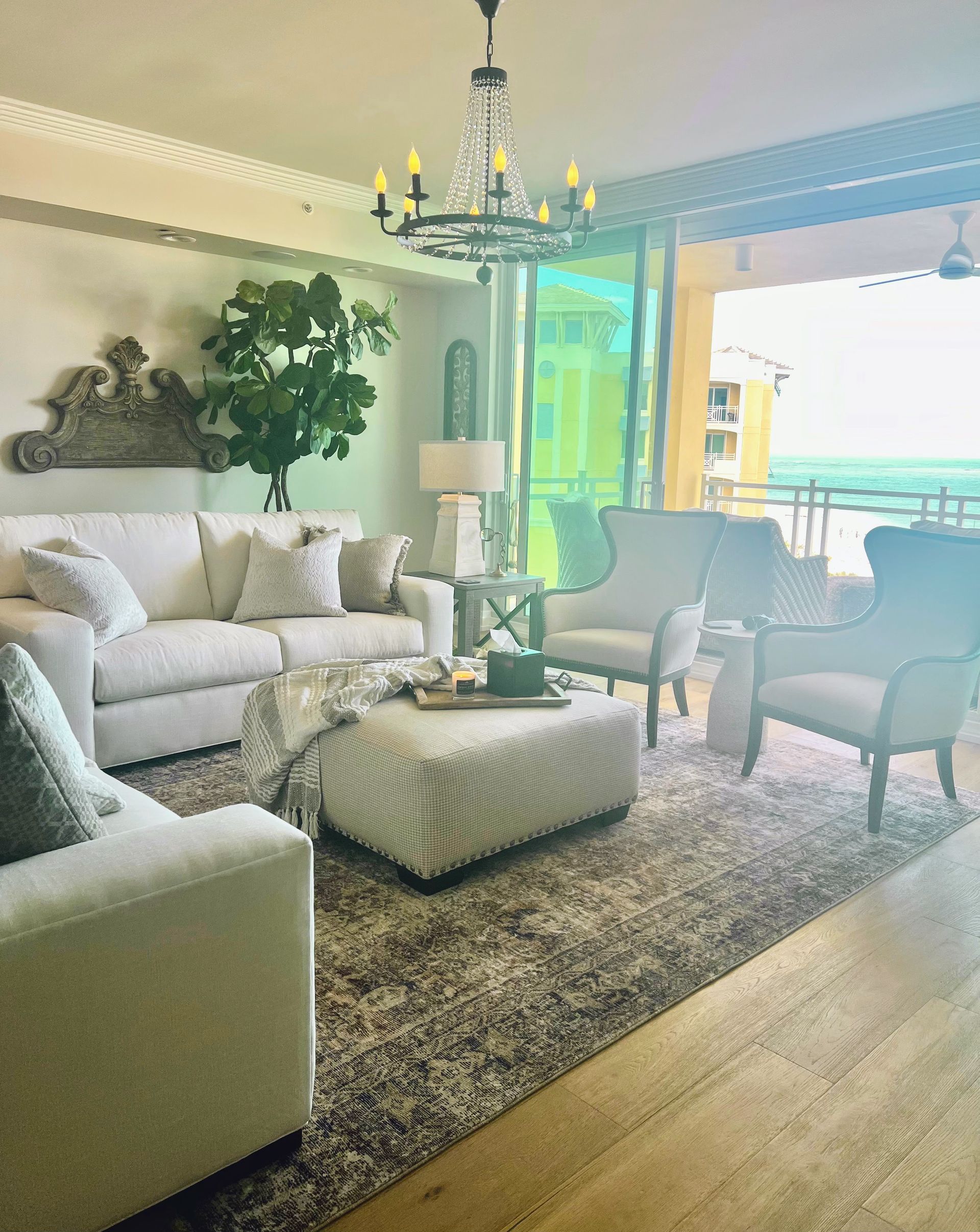 Elegant living room with white furniture, chandelier, and ocean view.