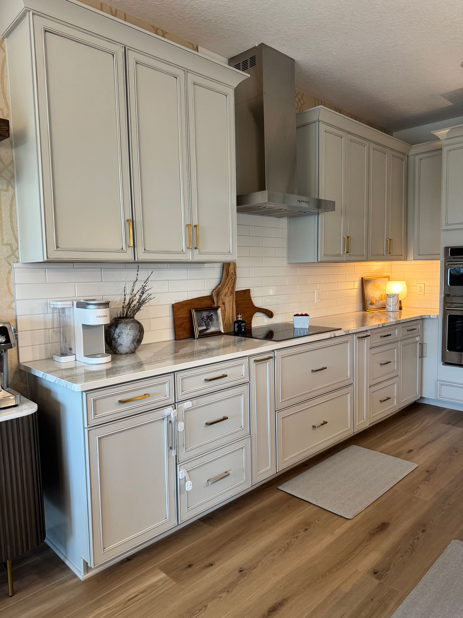 Kitchen with light gray cabinets, marble countertops, white backsplash, and wooden floors.