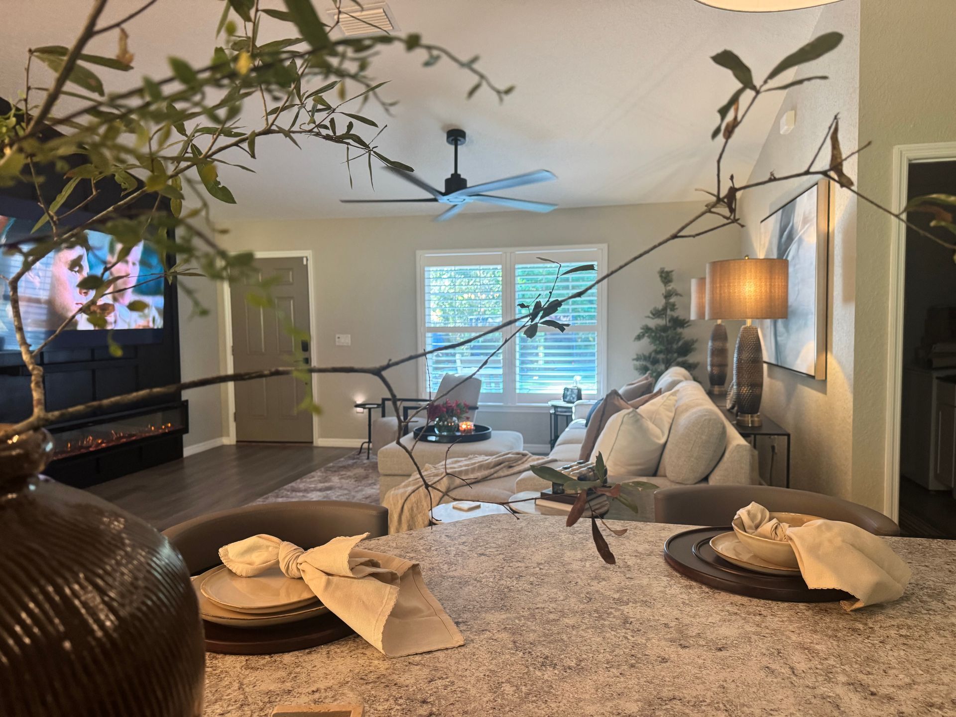 Living room interior with a decorated table in the foreground. Sofa, window, and TV visible.