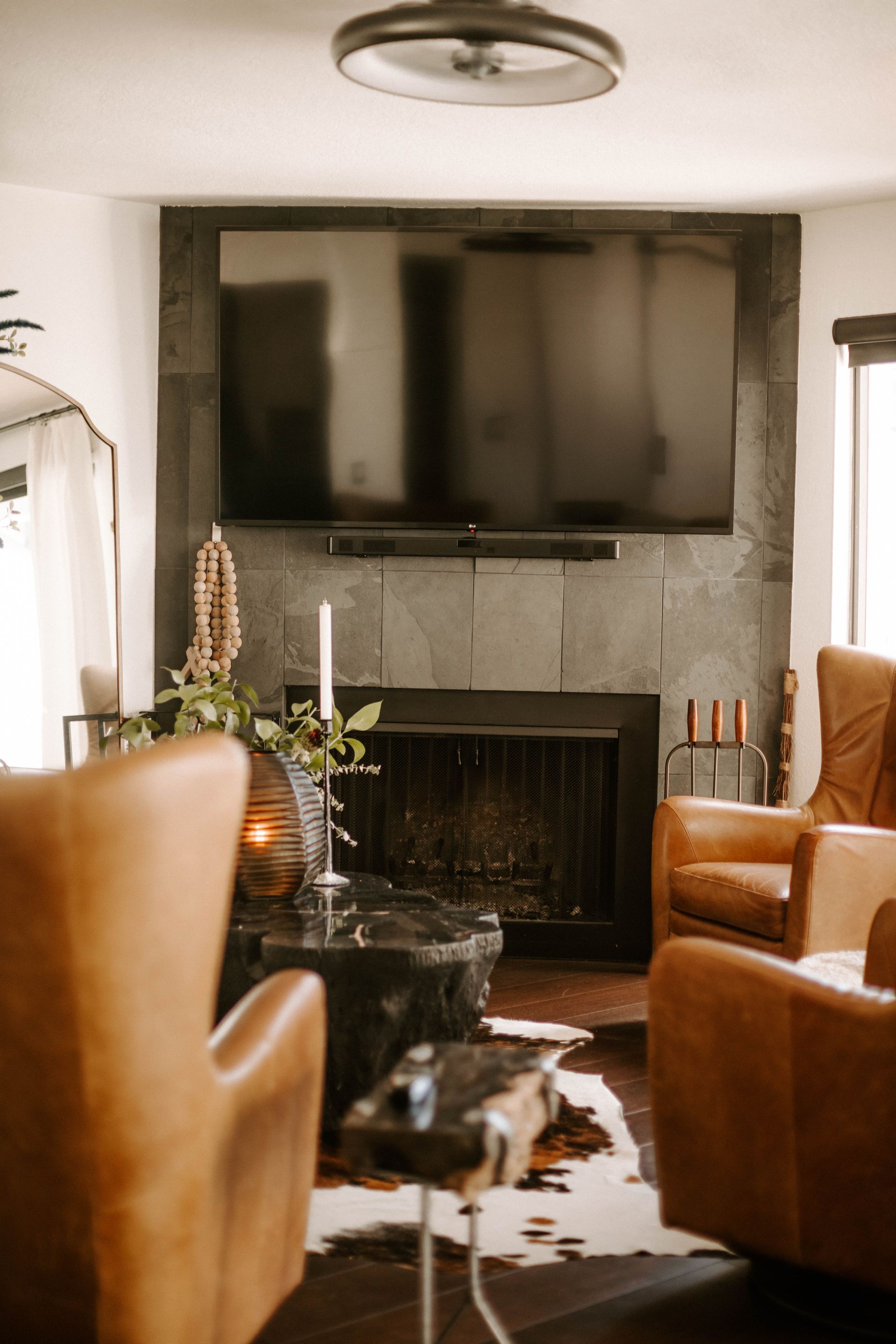 Living room with deer head art, leather chair, mirror with floral arrangement, and lit candles.