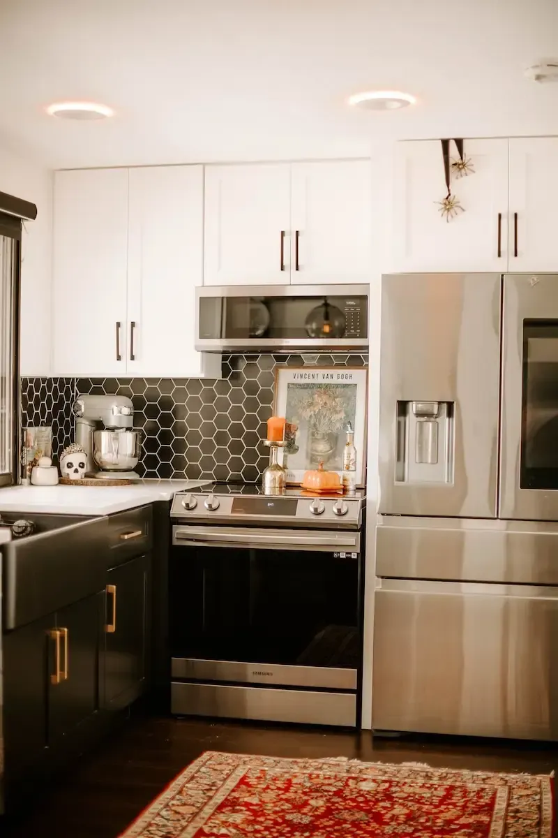 Kitchen with white and dark cabinets, stainless steel appliances, and a red rug.