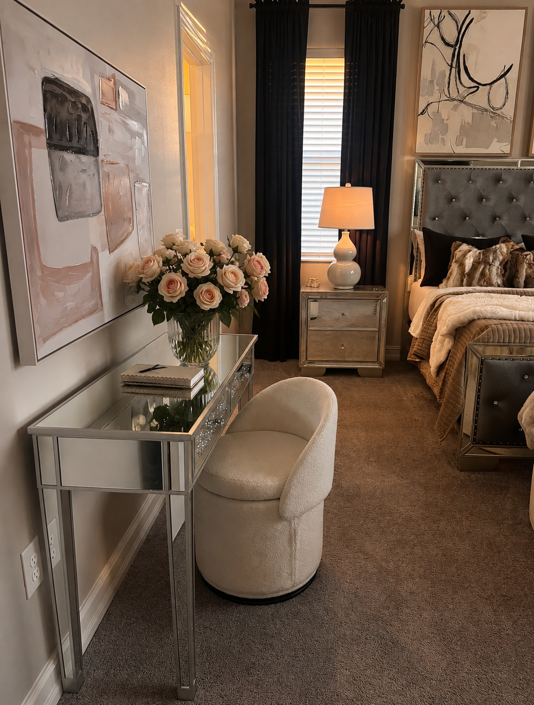 Elegant bedroom with mirrored vanity, floral decor, tufted bench, bedside lamp, and neutral bedding