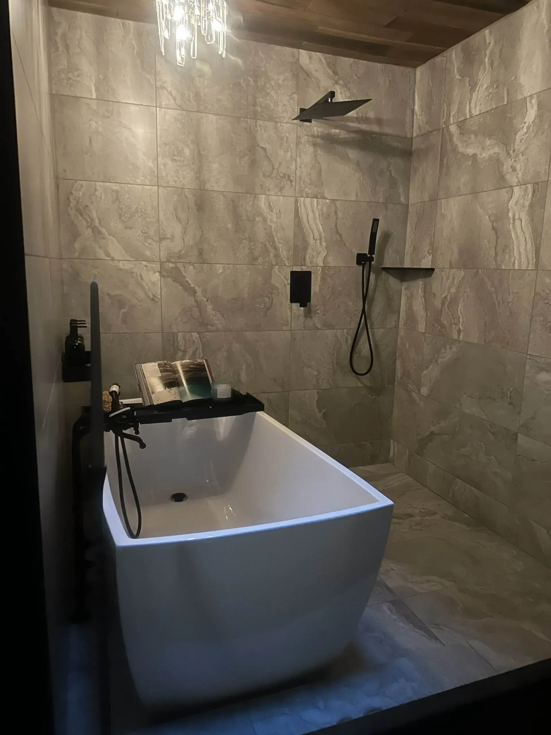Modern bathroom with white tub, gray tiled walls, black fixtures, and overhead shower.