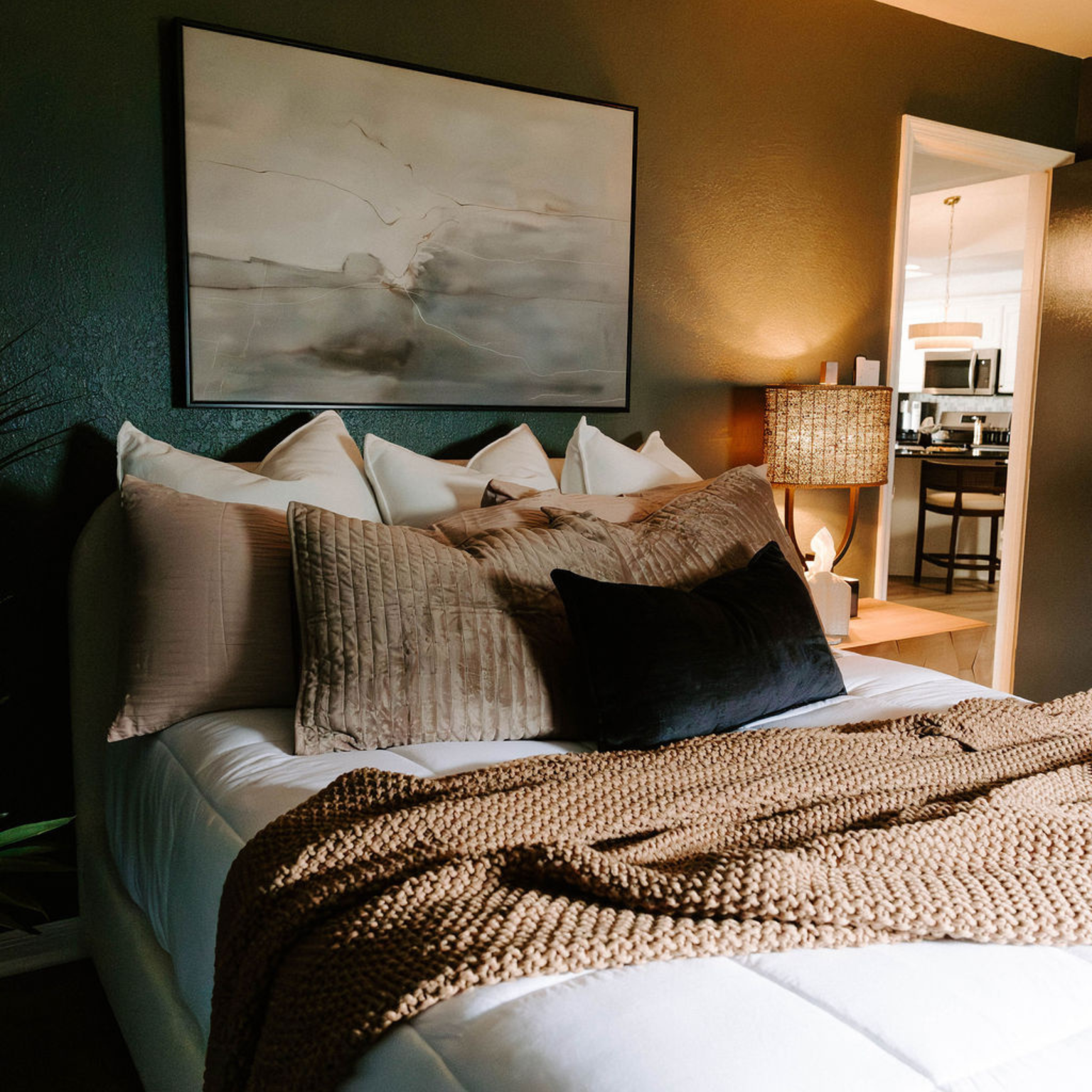 Cozy bedroom with a bed featuring a textured throw, pillows, and artwork on a dark green wall.