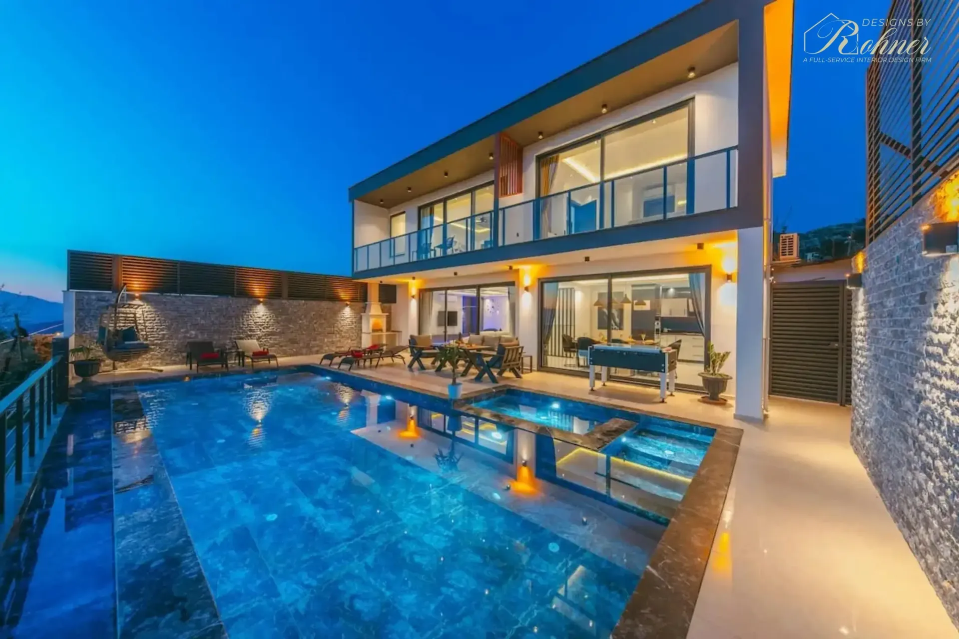 Modern villa with a pool, illuminated at dusk. Features balconies, dining area, and mountain view.