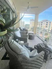 Balcony with wicker furniture, ocean view, white cushions, plants.