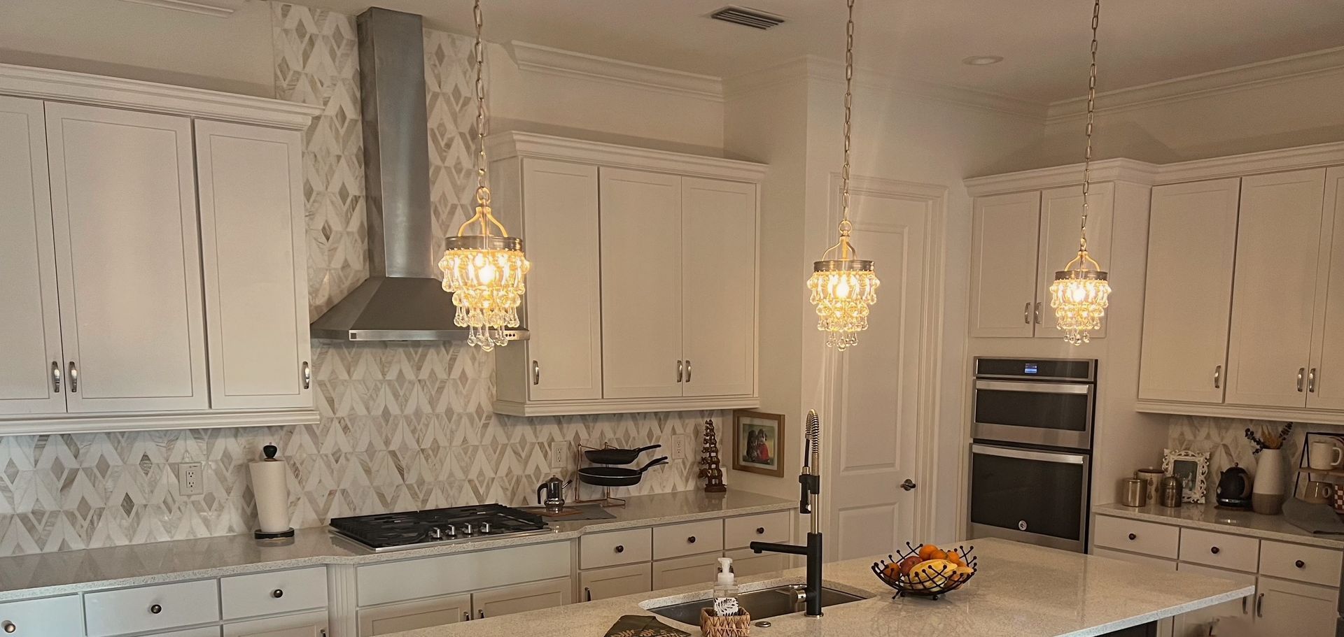 Bright, white kitchen with crystal pendant lights. Stainless steel range hood and white cabinetry.