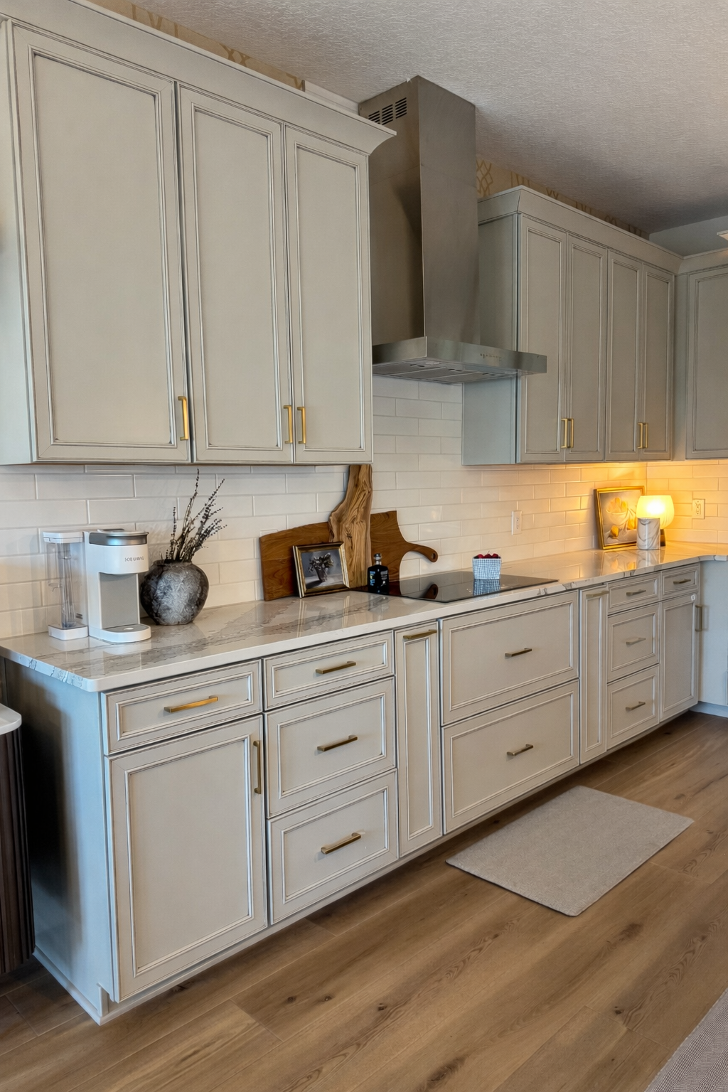 Kitchen with light gray cabinets, marble countertops, stainless steel range hood, and wood flooring.