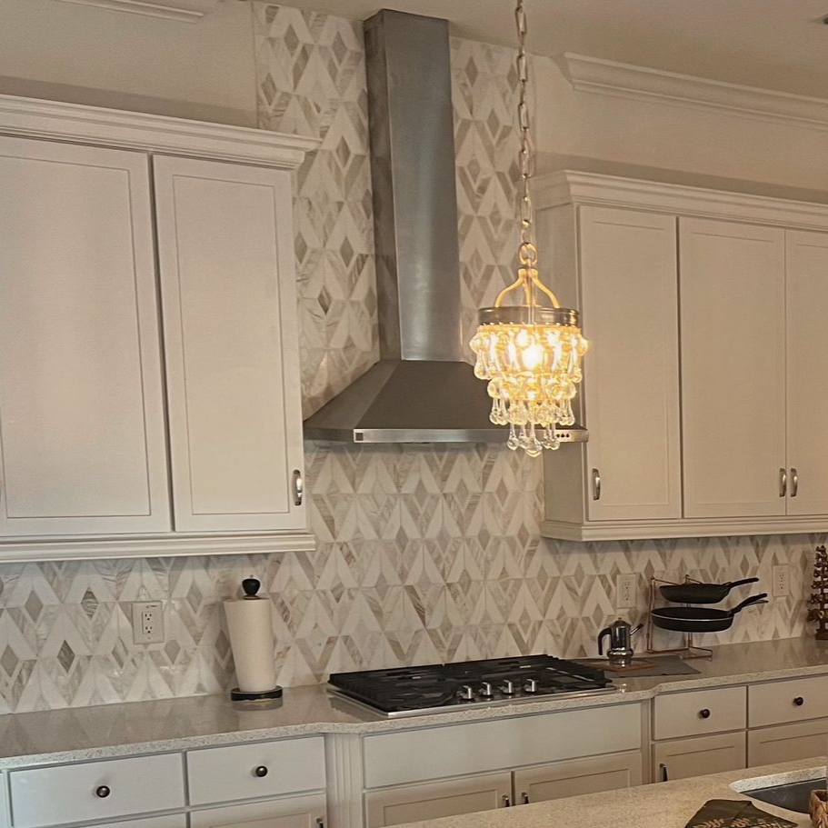 Kitchen with white cabinets, patterned backsplash, range hood, and chandelier.