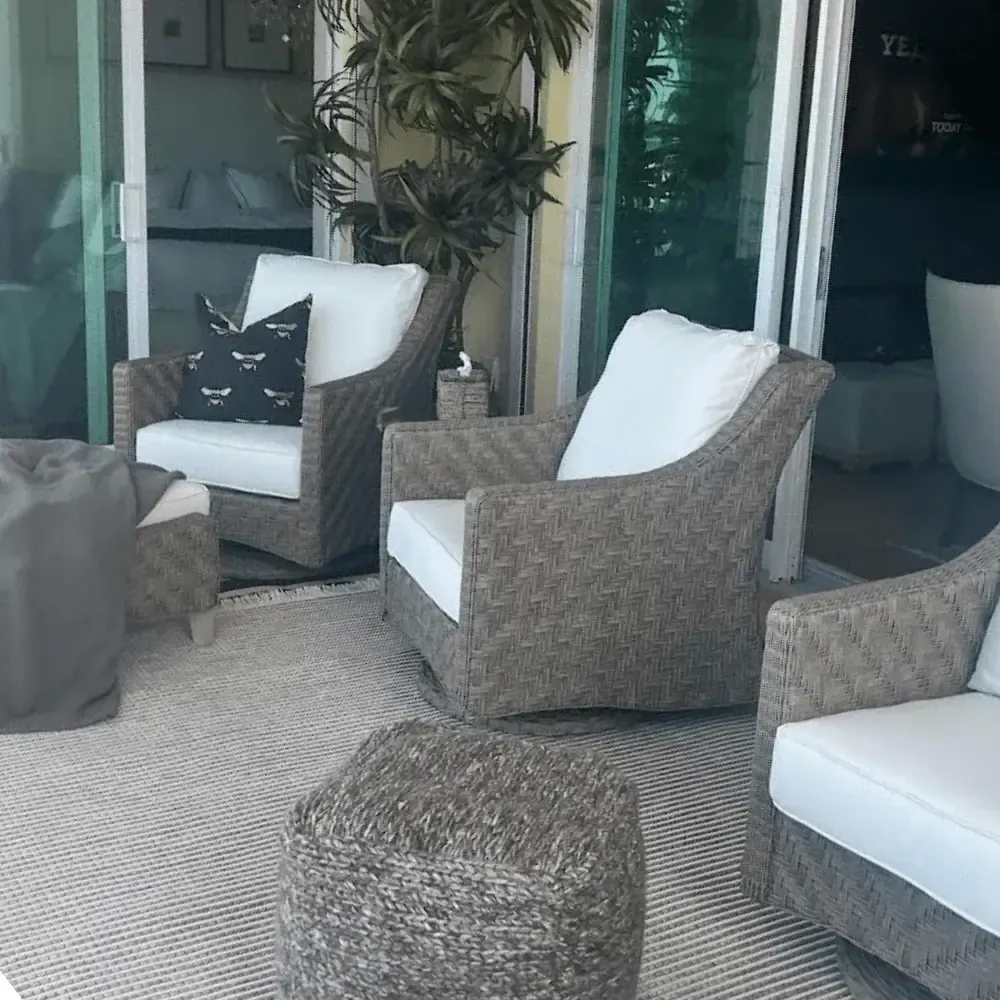 Outdoor seating area with wicker chairs and white cushions on a patterned rug.