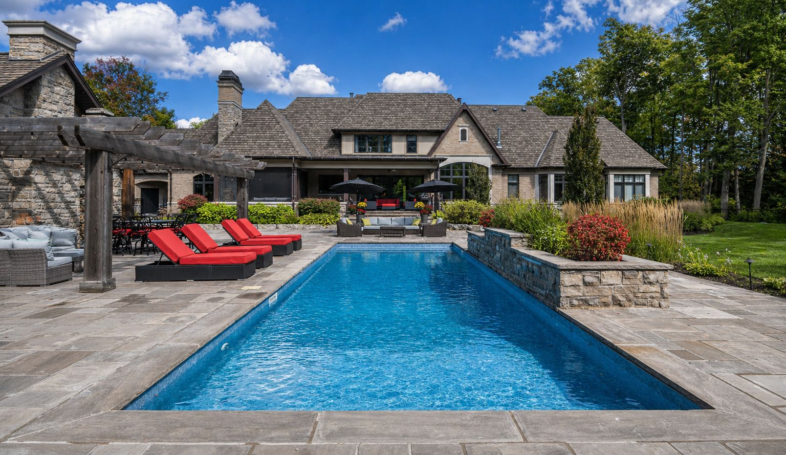 Luxury stone house with a turquoise pool, red loungers, and a landscaped patio under a blue sky