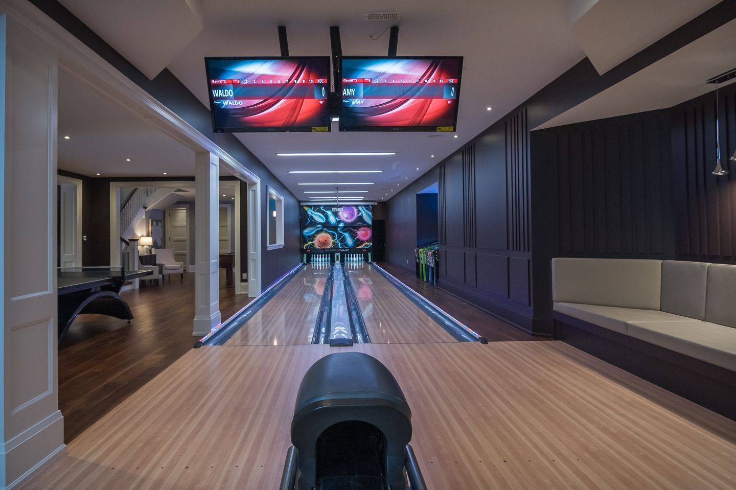 Bowling alley with wooden lanes, two screens, and floral wall art.