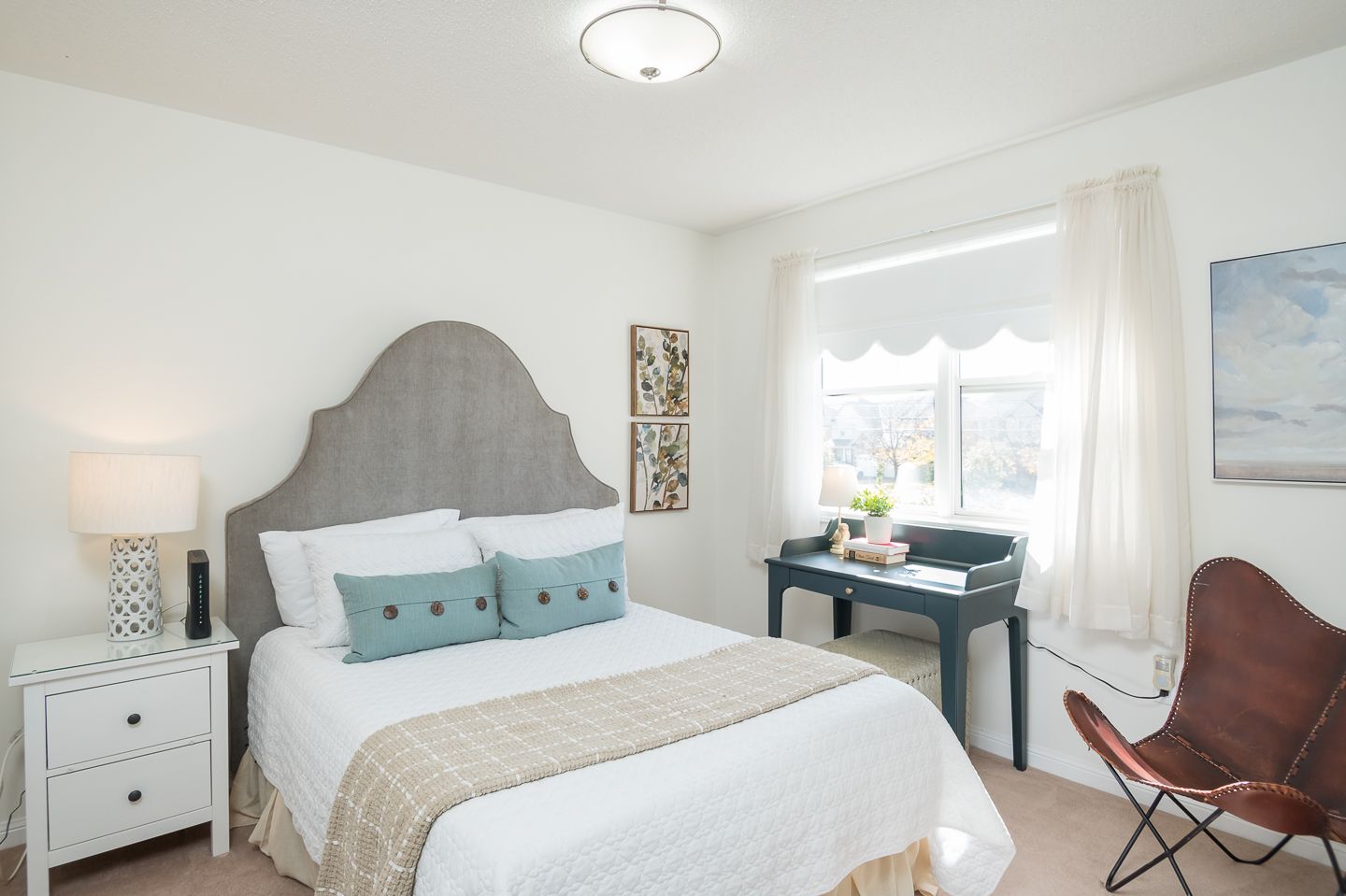 Bedroom with a gray headboard, white bedding, teal pillows, and a small desk.