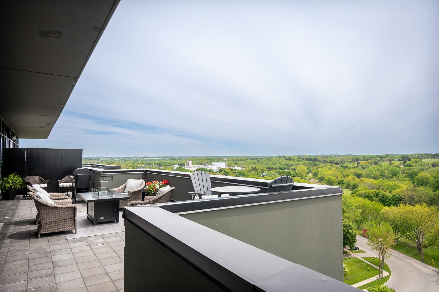 Rooftop patio with wicker furniture, views of trees and buildings under a cloudy sky.