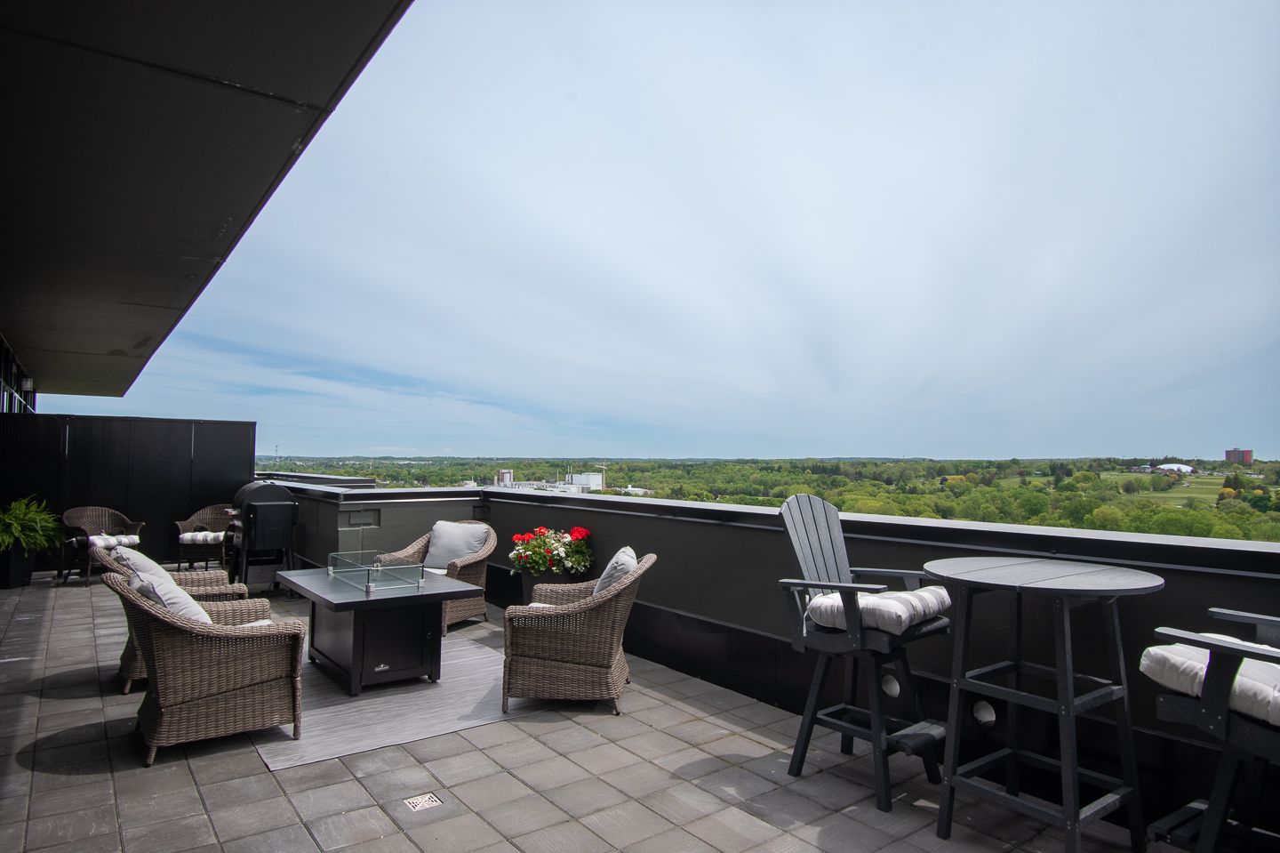 Rooftop patio with seating, fire pit, and a scenic view of trees and sky.