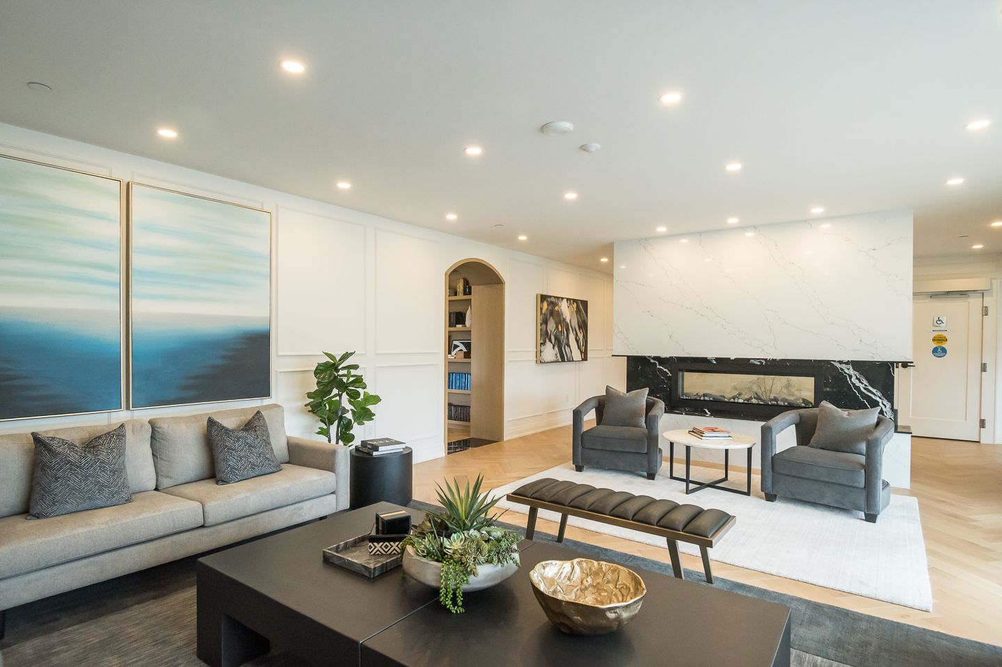 Spacious living room with modern decor: gray sofa, armchairs, fireplace, art, and light wood floors.