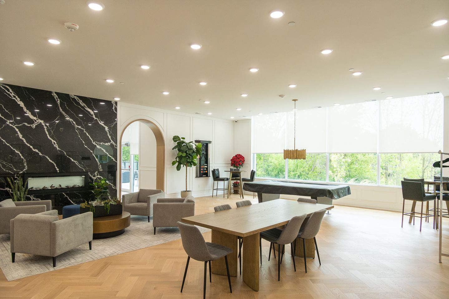 Spacious lounge area with seating, a pool table, fireplace, and dining table, lit by recessed lighting.