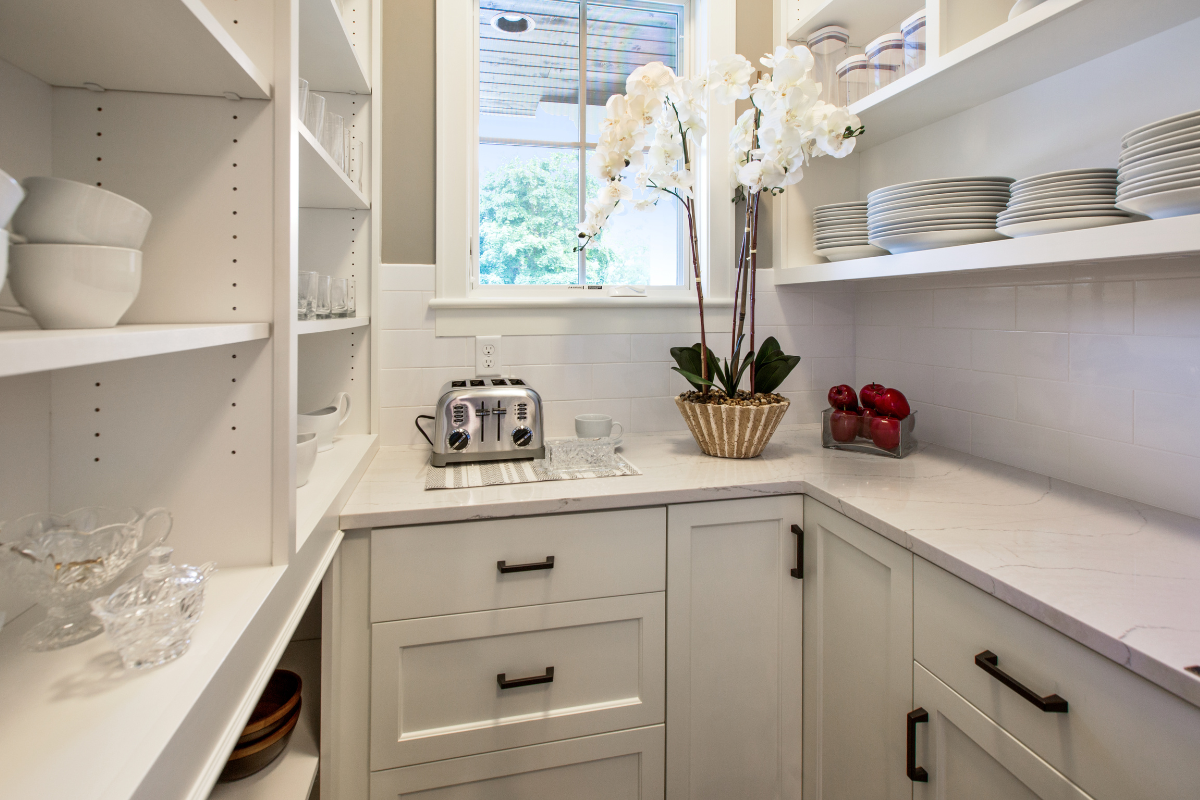 A kitchen pantry with white cabinets , shelves , drawers and a toaster oven.