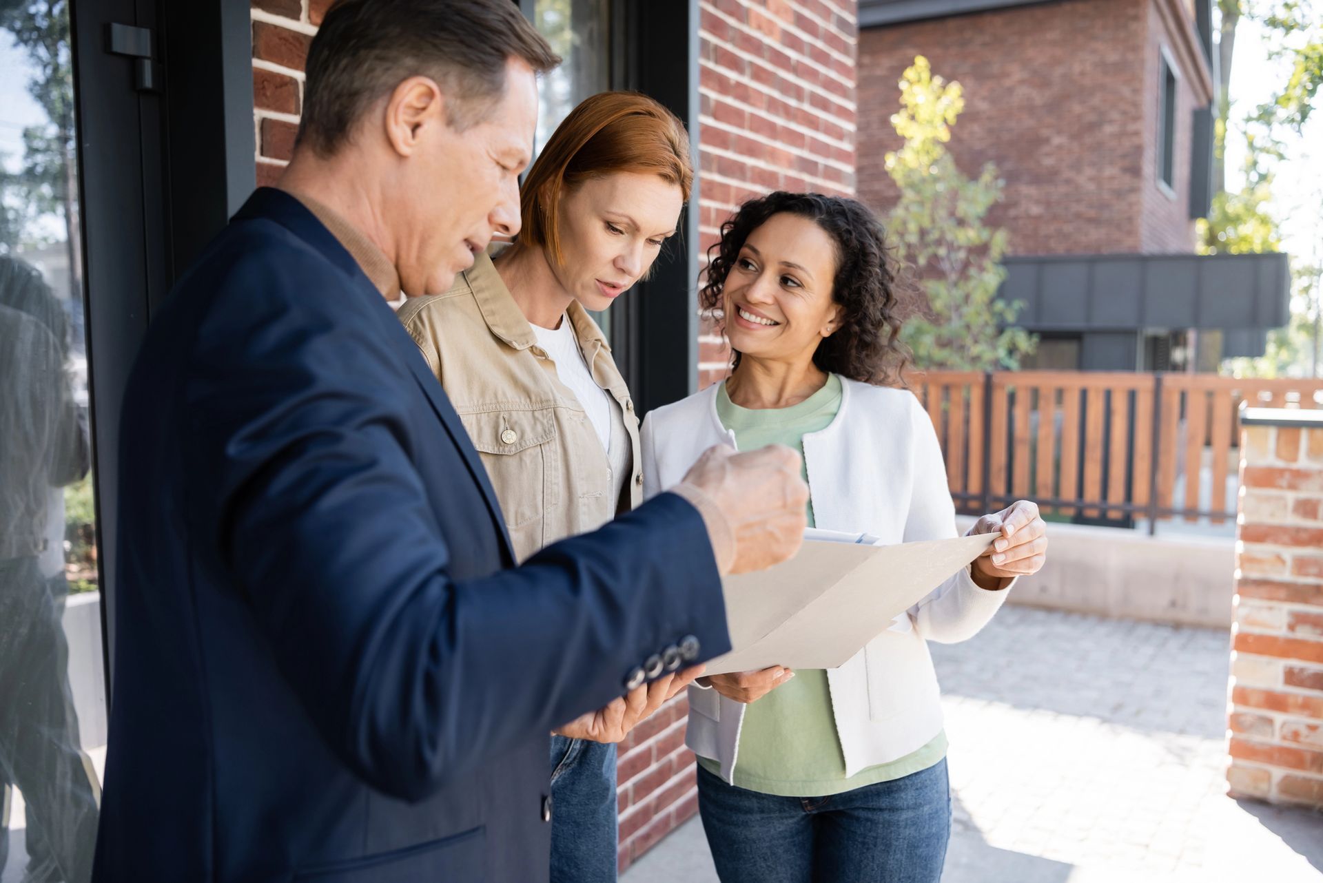 A man in a suit is talking to two women in front of a brick building.