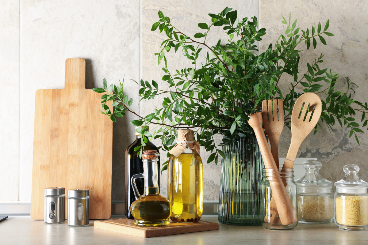 A kitchen counter with utensils , cutting boards , bottles of olive oil and herbs.