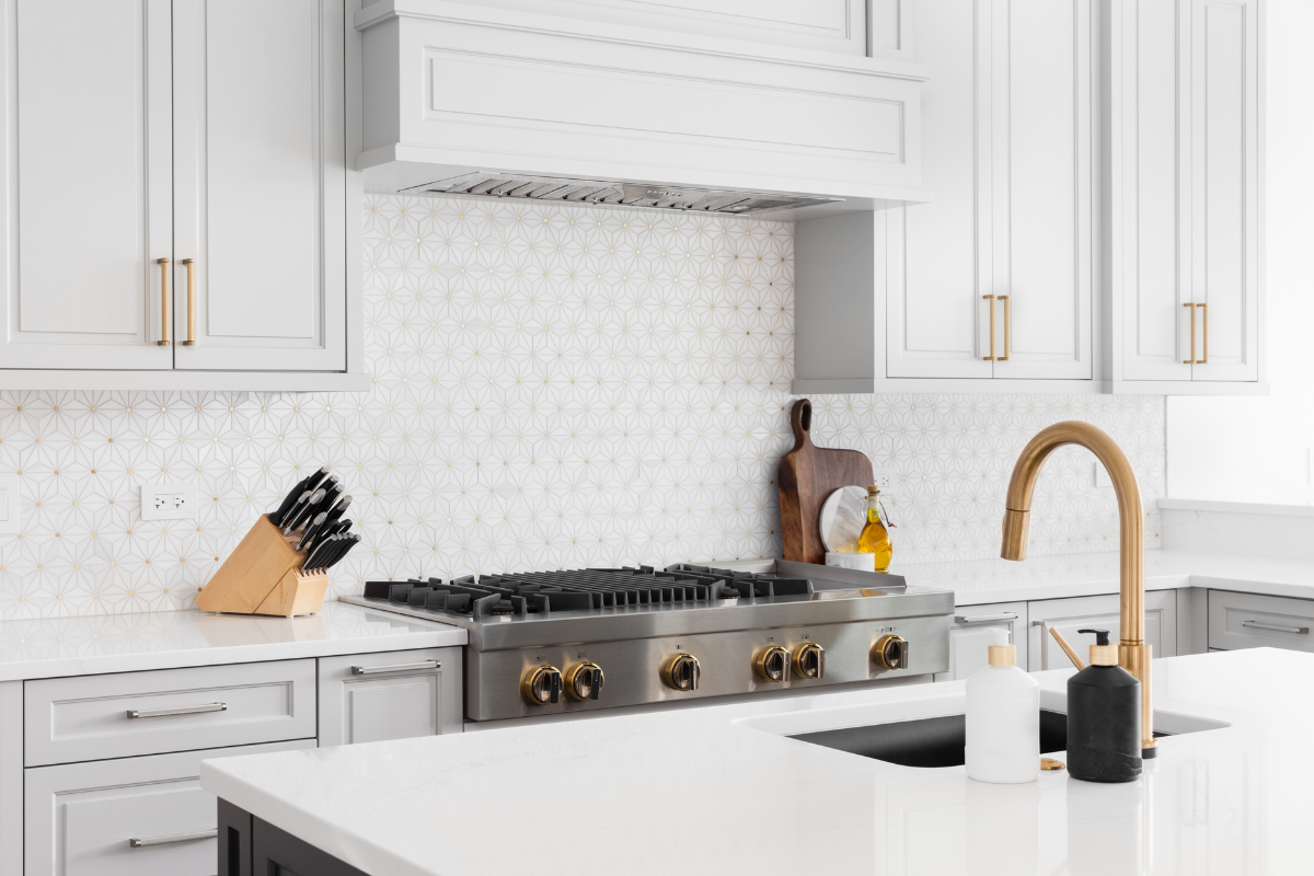 A kitchen with white cabinets , a stove , a sink , and a faucet.