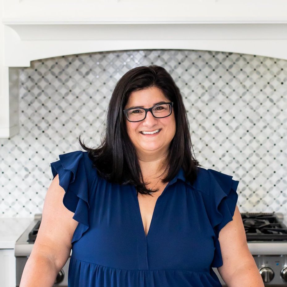A woman wearing glasses and a blue dress is smiling in a kitchen.