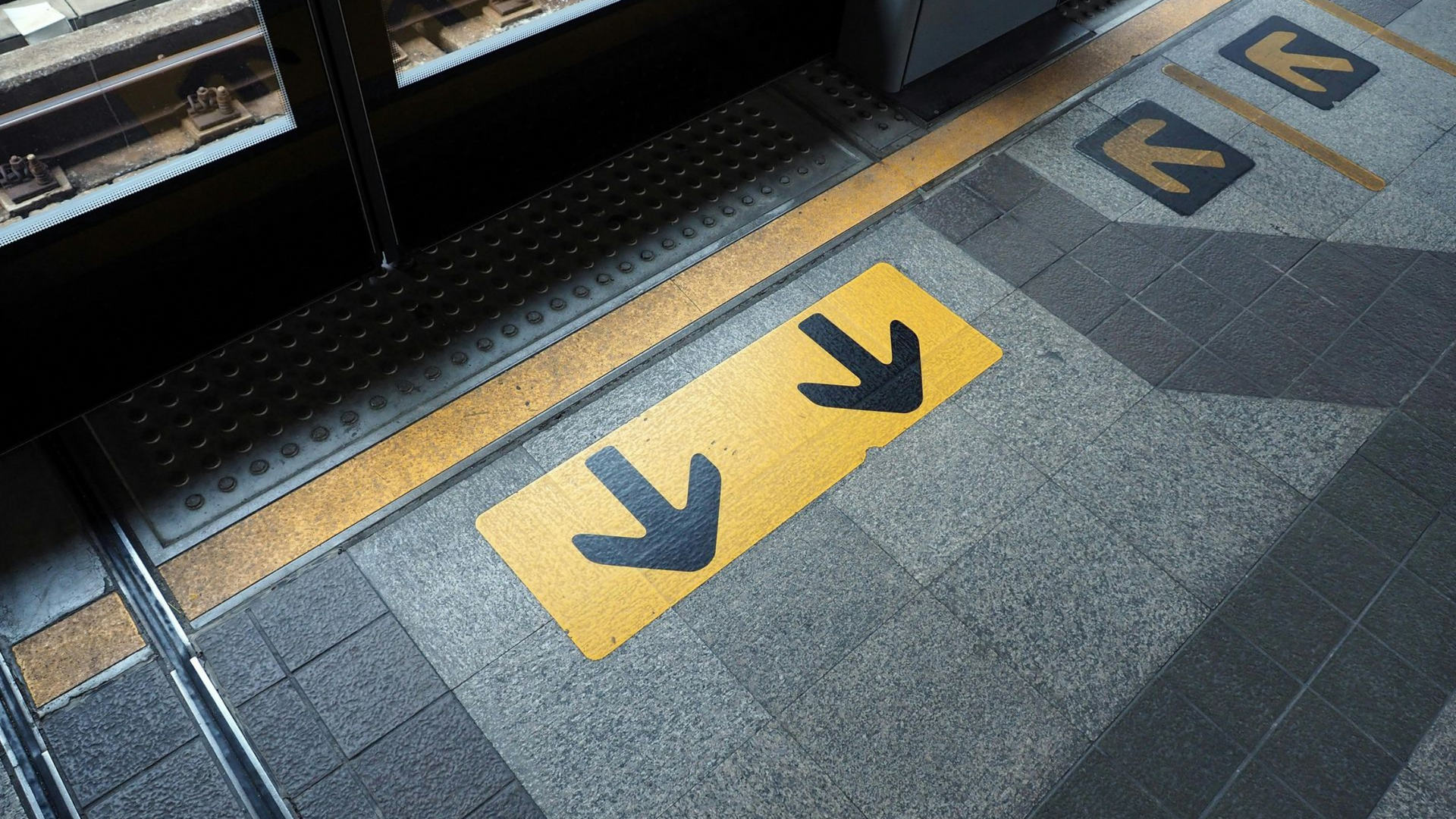 Yellow floor markings with directional arrows on a subway platform next to the tracks.