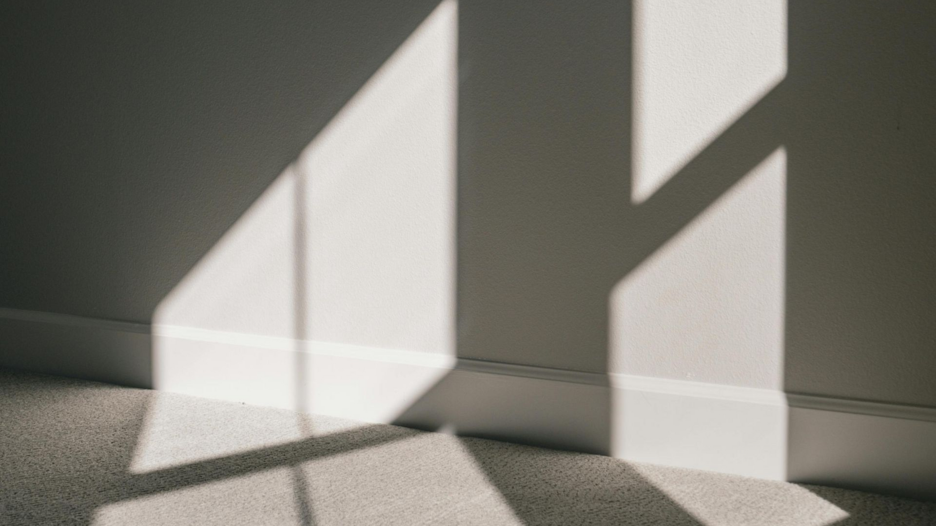 Shadows of sunlight on a white wall and carpet, creating shapes.