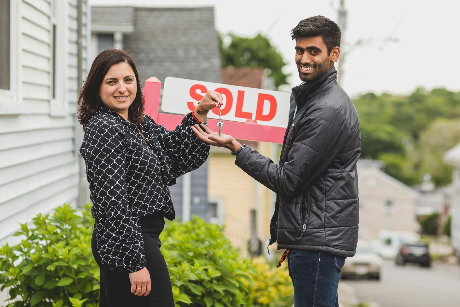 Woman handing keys to a man in front of a house with a 