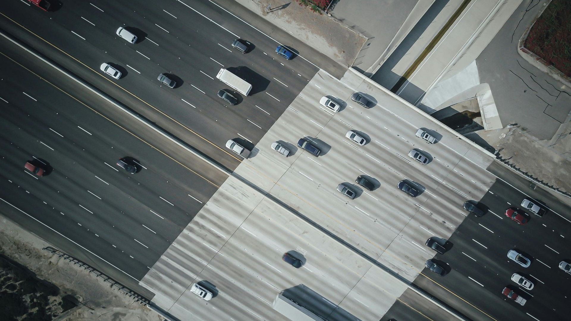 Aerial view of cars traveling on a multilane highway crossing over a bridge, with asphalt and concrete road segments.