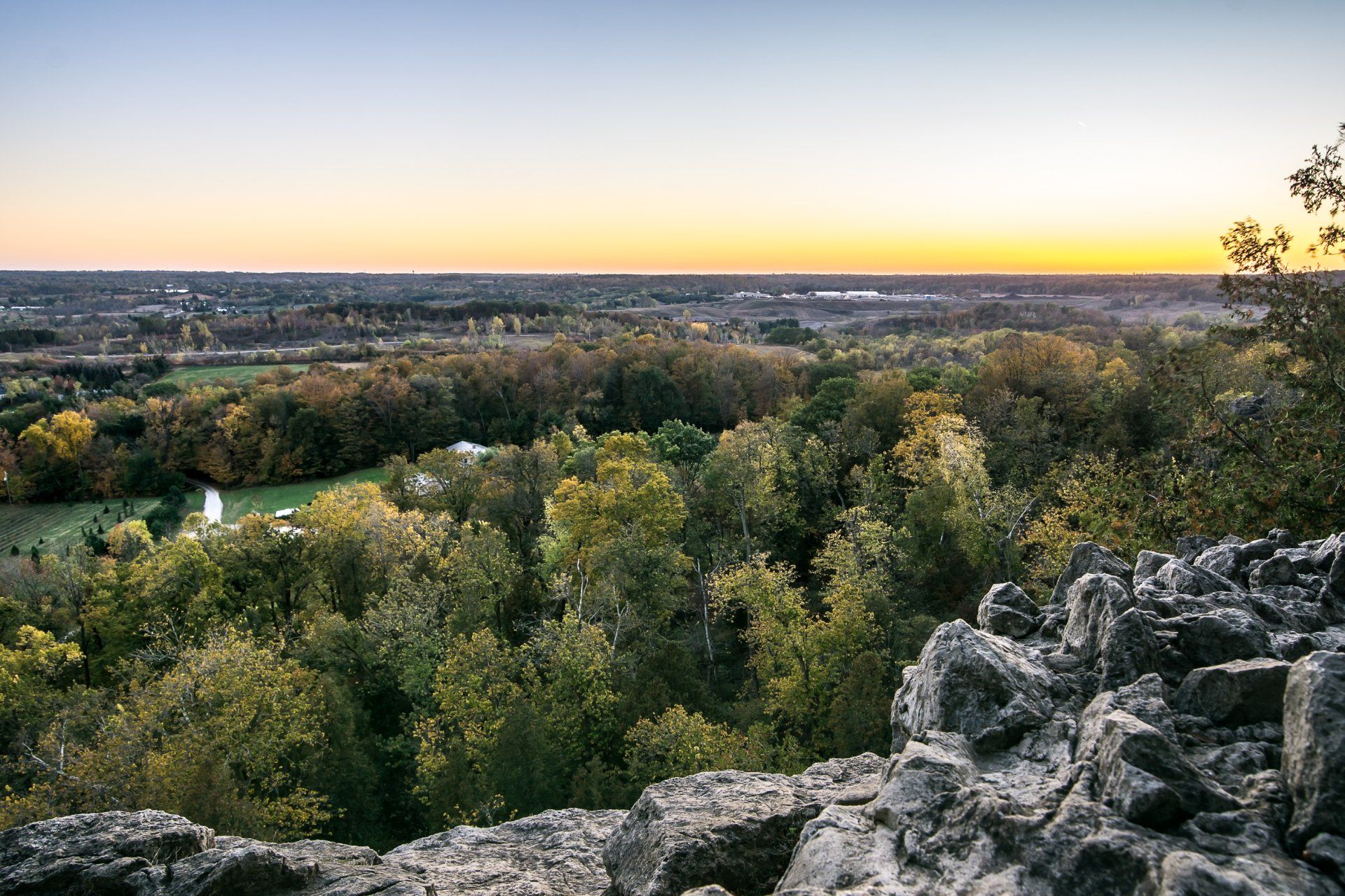 A view of a forest from a rocky cliff at sunset.