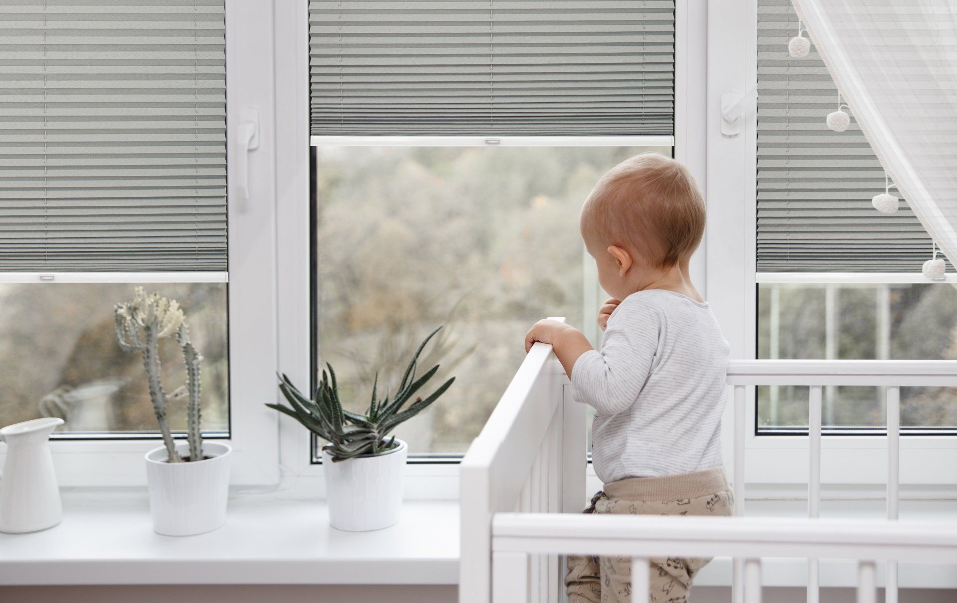 Ein Baby steht in einem Kinderbett und schaut aus dem Fenster.