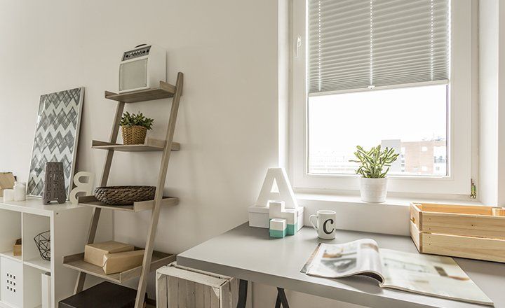 Ein Schreibtisch mit einem Buch darauf vor einem Fenster in einem Zimmer.