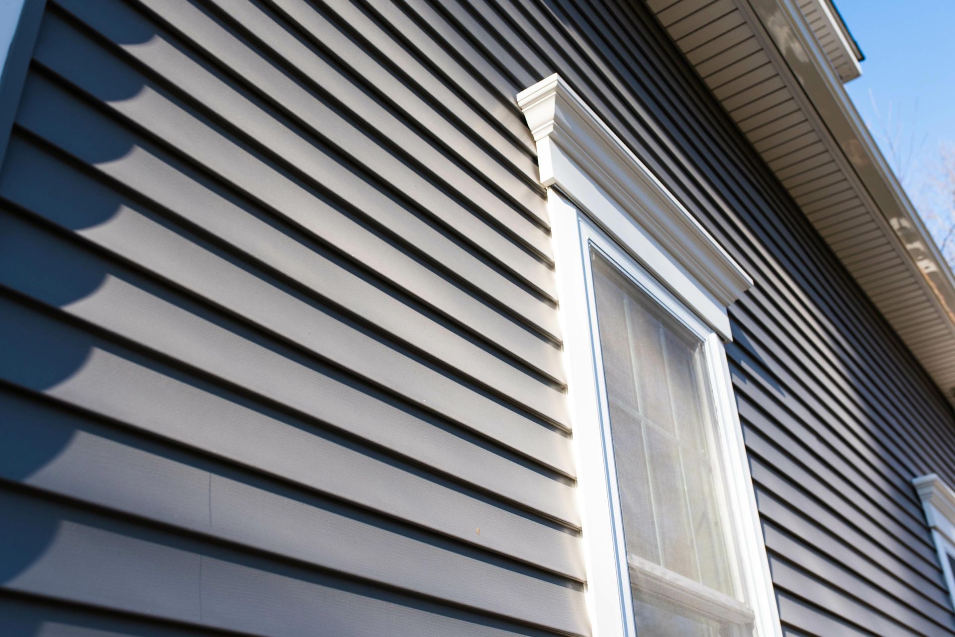 A close-up view of a house exterior with gray vinyl siding and a white-framed window