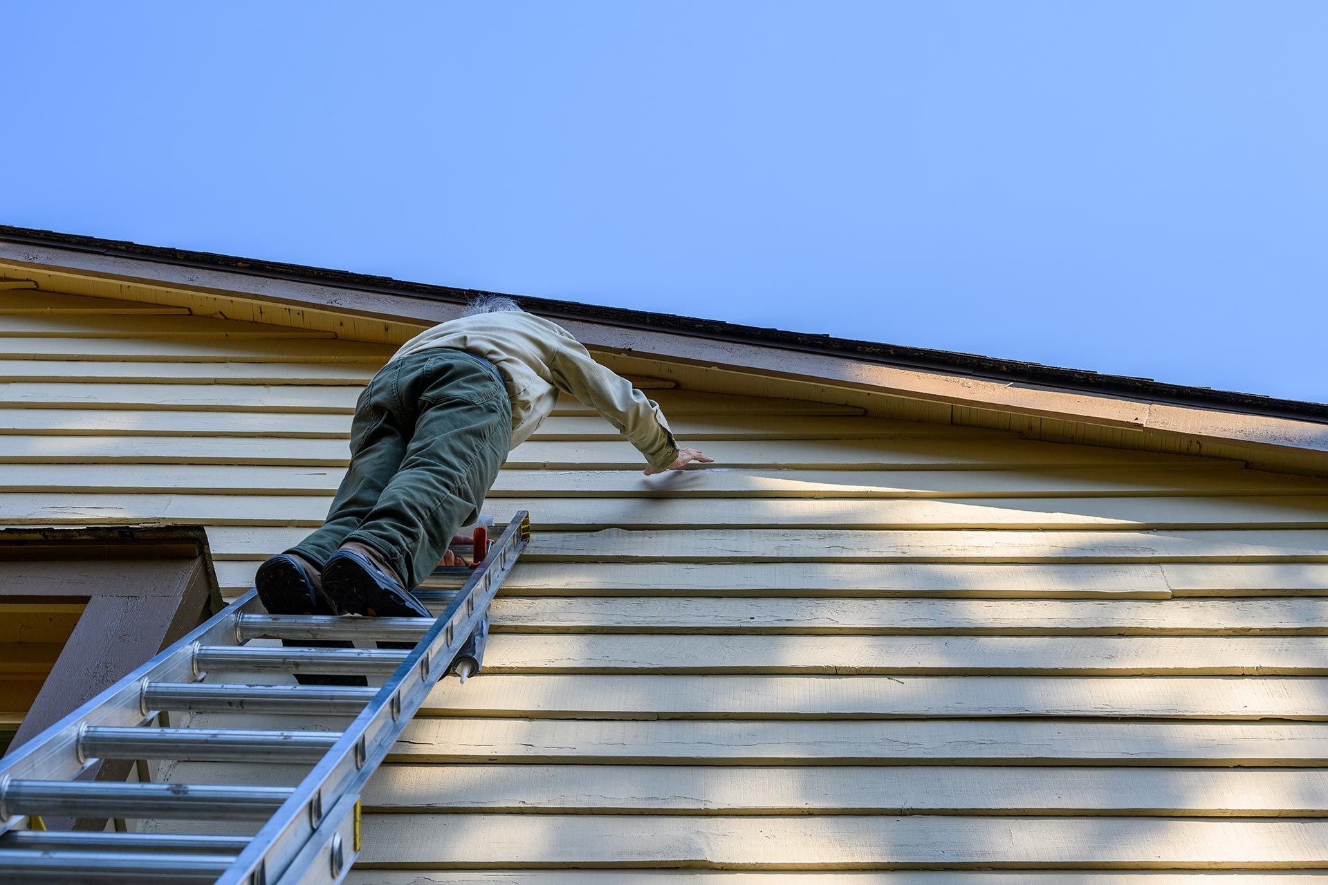 Person on a ladder inspecting siding on the upper exterior of a house.