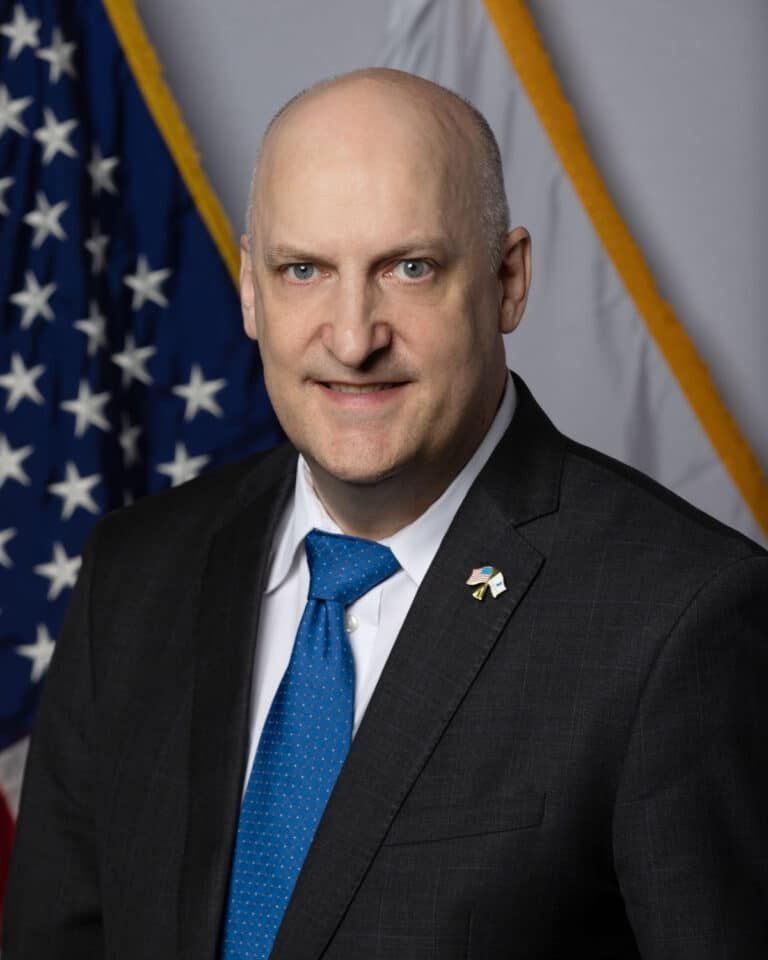 A man in a suit and tie is standing in front of an american flag.