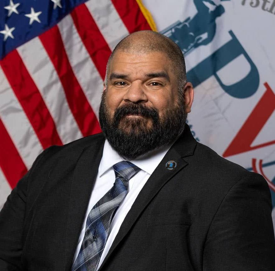 A man in a suit and tie is standing in front of an american flag.