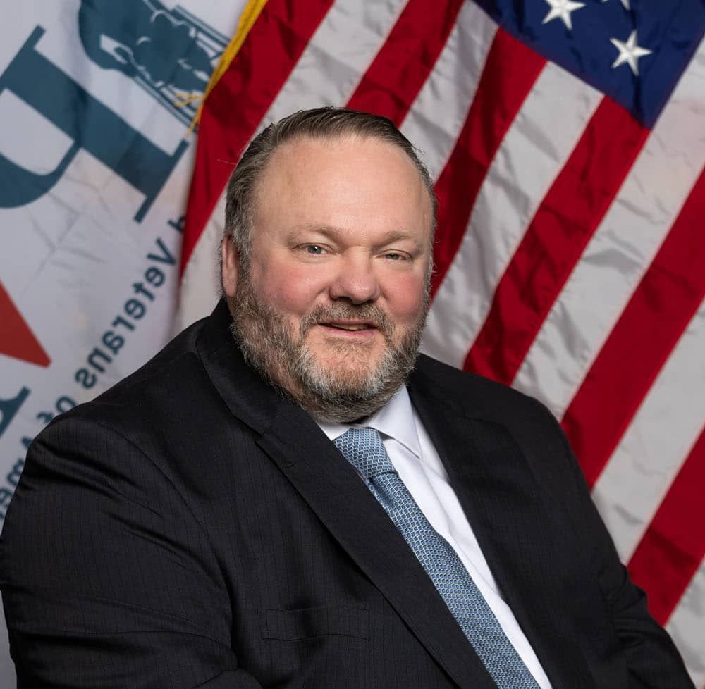 A man in a suit and tie is sitting in front of an american flag