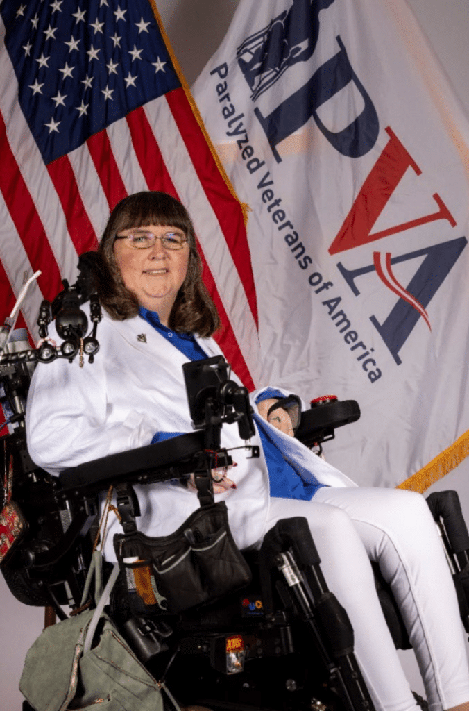 A woman in a wheelchair is standing in front of an american flag.